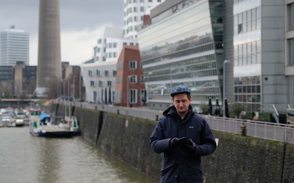 Martin Balogh steht mit Handy in der Hand am düsseldorfer Hafen.